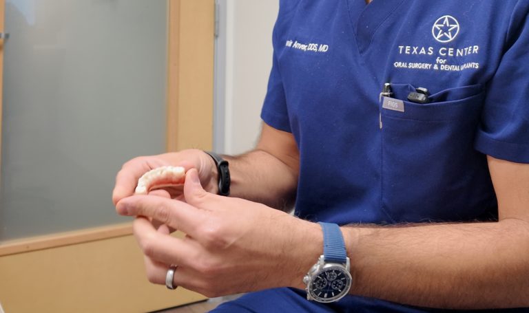 Oral surgeon holding a fixed full arch dental implant prosthesis while explaining treatment options for full arch tooth replacement.